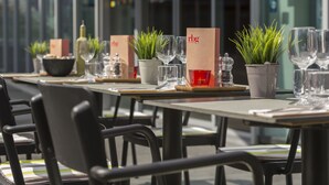 Une rangée de tables aménagées avec des plantes en pot, des verres à vin et des menus, dans un espace de restauration en plein air.