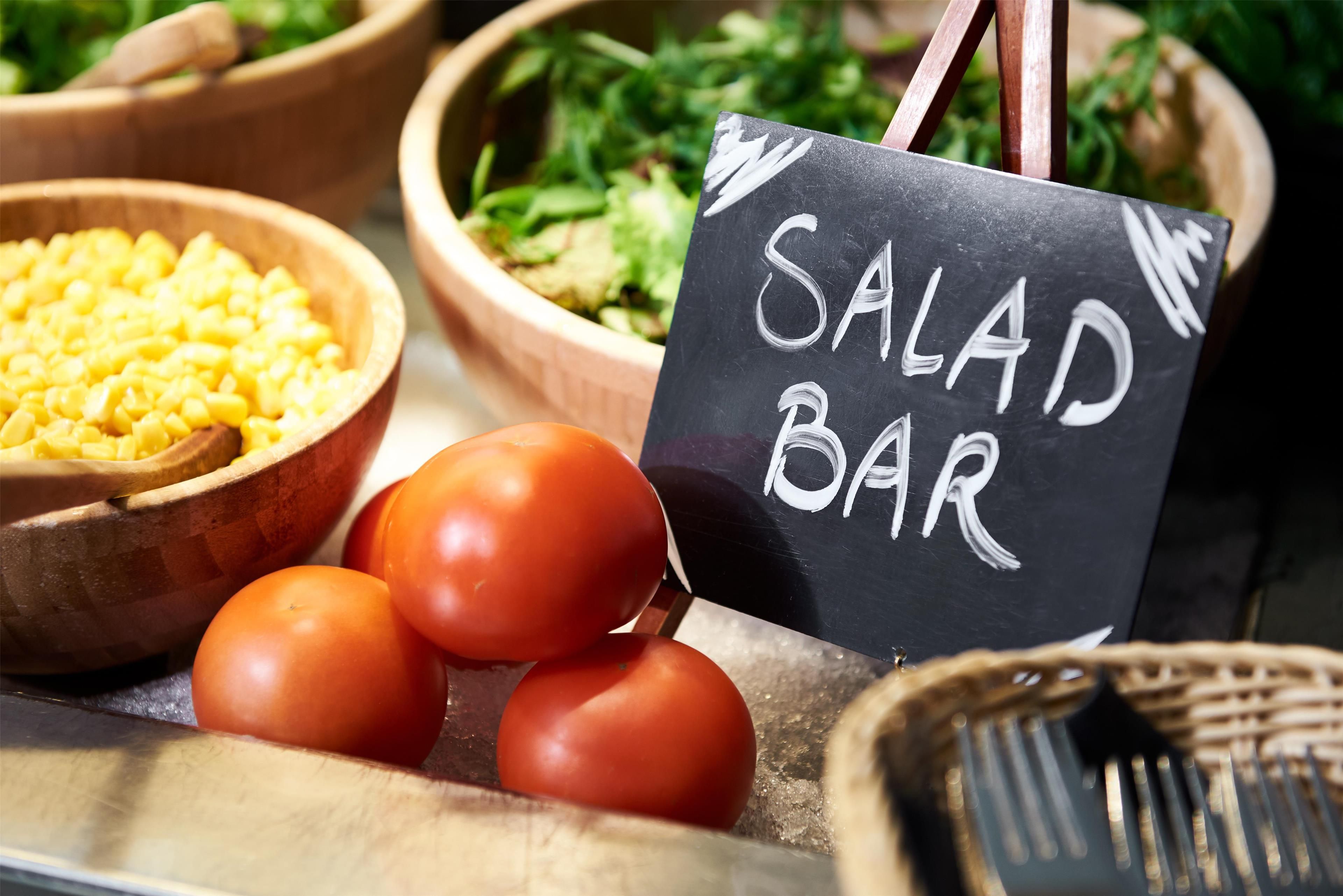 A salad bar with various vegetables and a sign indicating the type of food available.