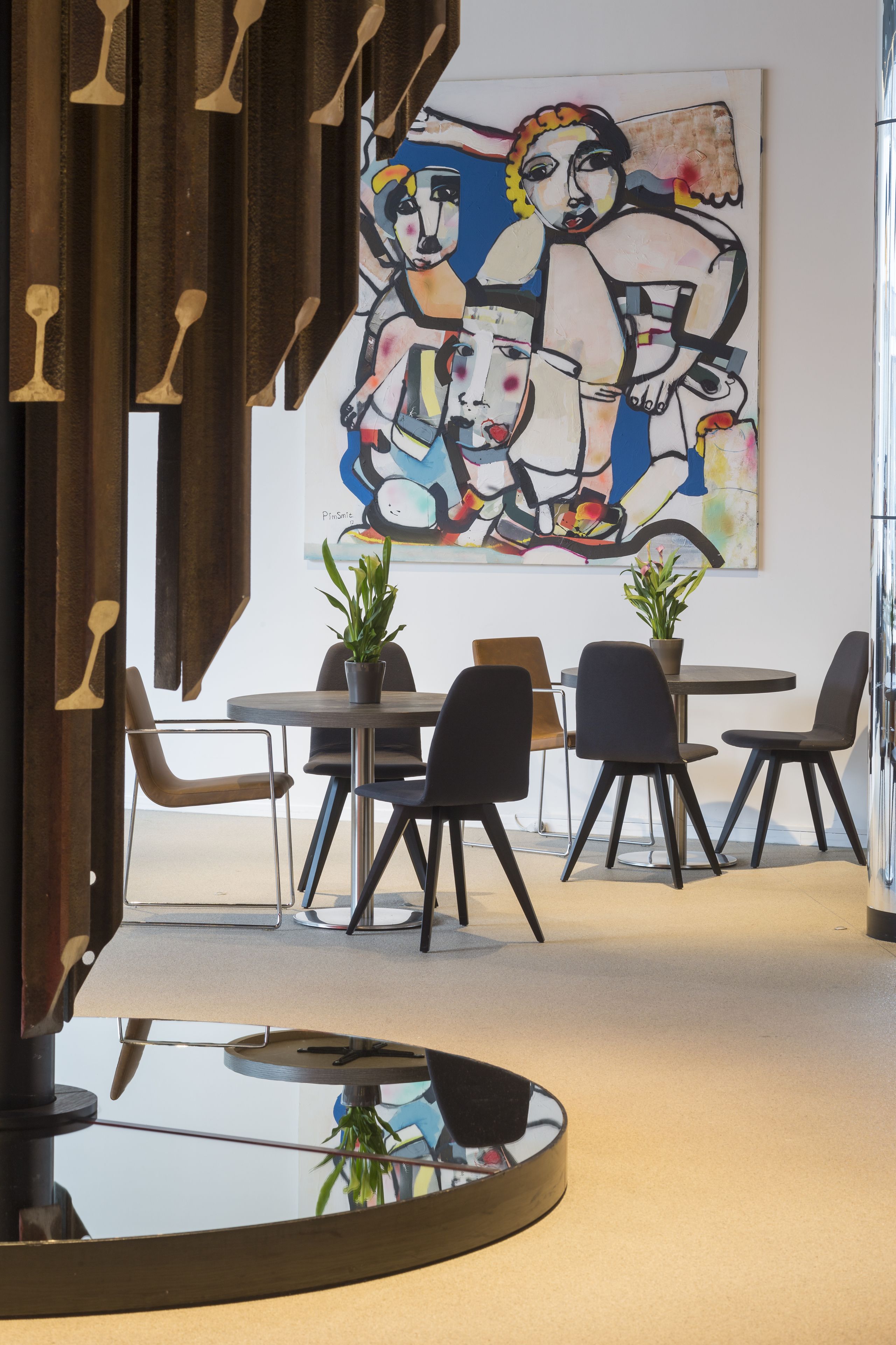 A modern dining area with a glass table, black chairs, and a potted plant. A large abstract painting is on the wall.