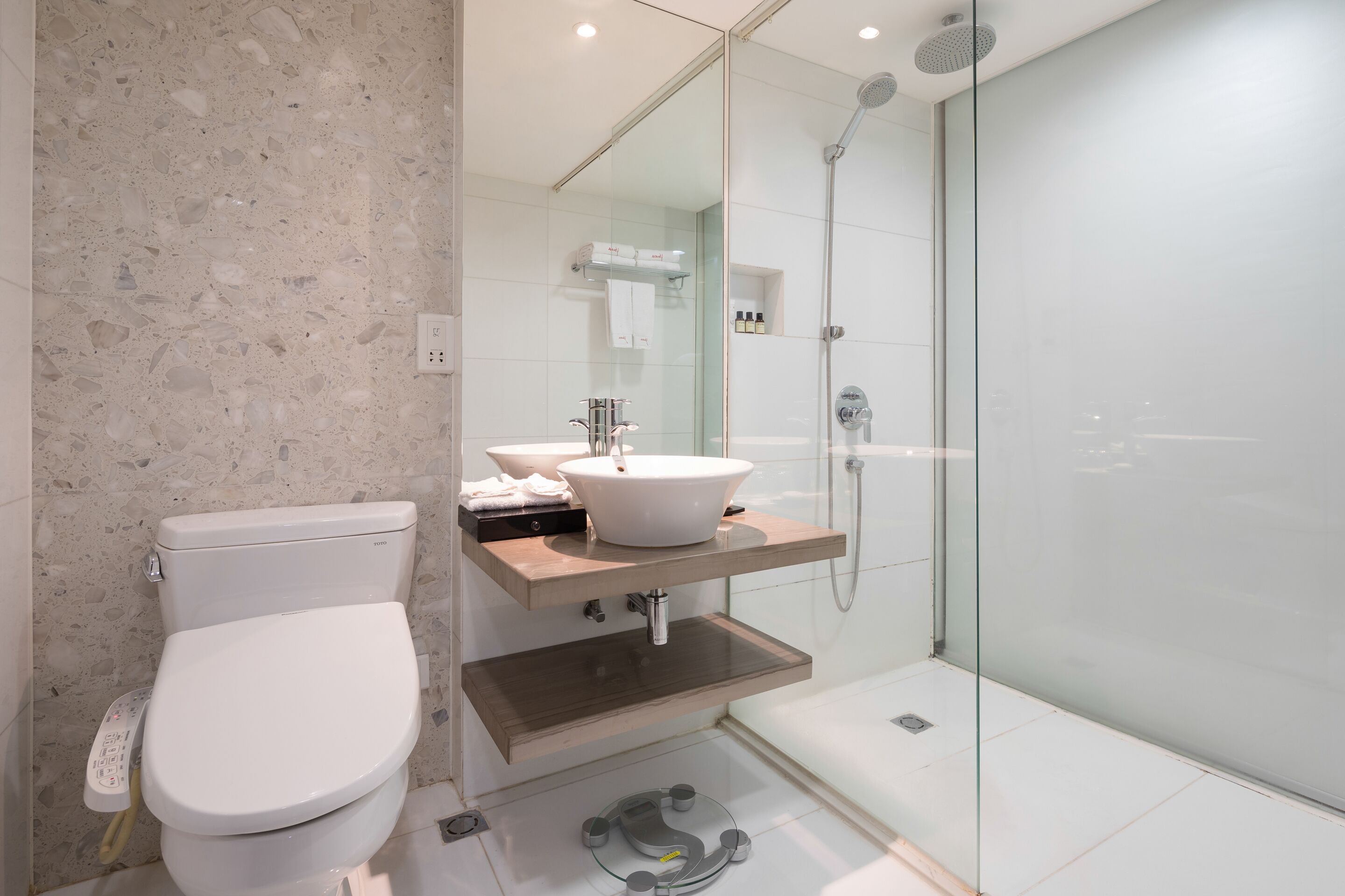 A modern bathroom with a freestanding toilet, a vessel sink, and a glass-enclosed shower area.