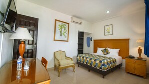 Una habitación de hotel con cama, una silla, una mesa con lámpara, televisión y escritorio.