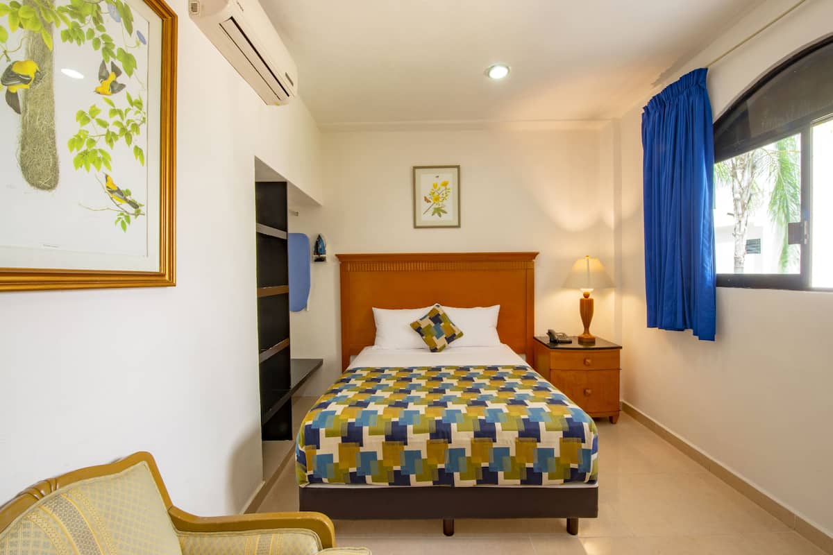 A hotel room with a bed, a nightstand, a lamp, a chair, and a window with curtains.