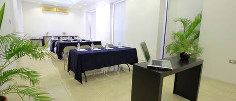 Un salón de conferencias con mesas, sillas y un ordenador portátil sobre un escritorio.