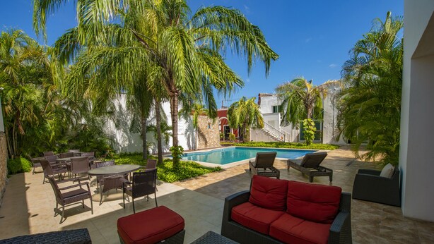 Un patio con mobiliario de mimbre, piscina y palmeras.