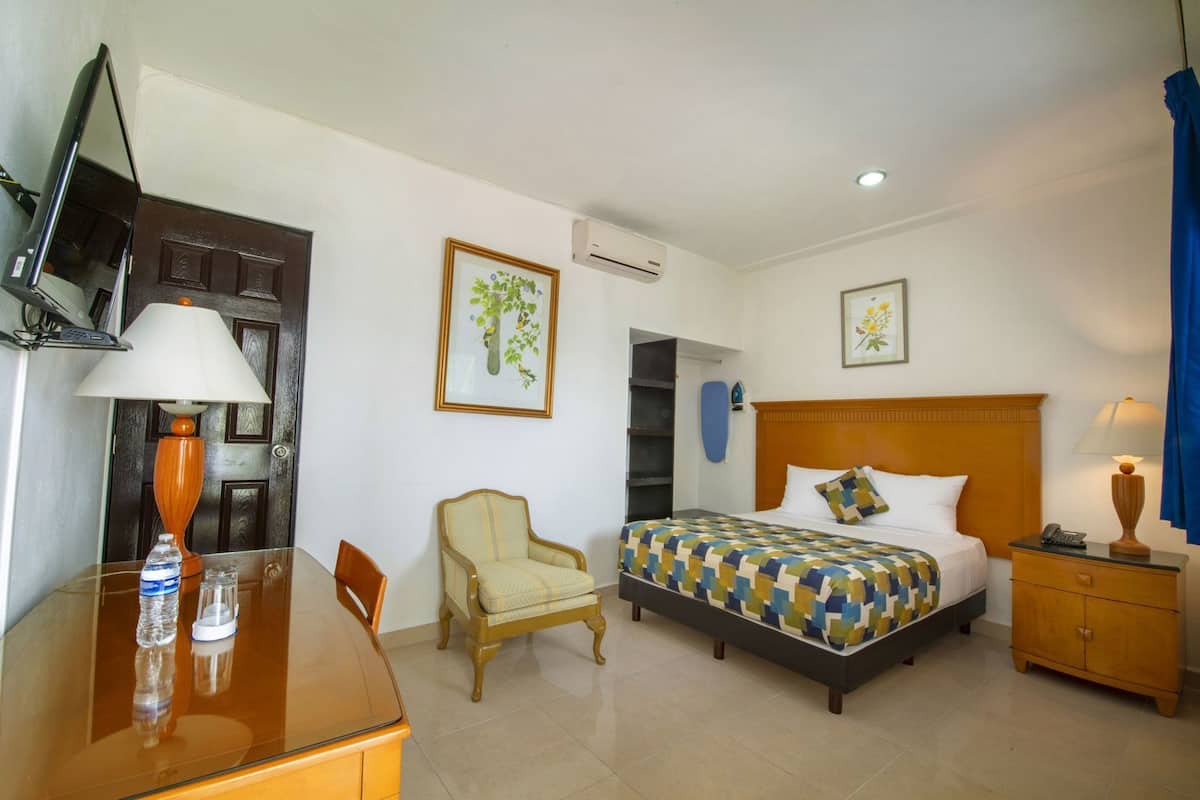 A hotel room with a bed, a chair, a desk, a TV, and a door.