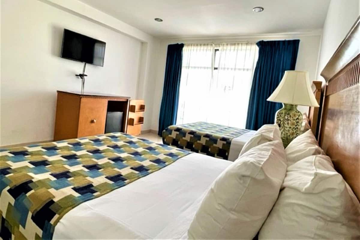 A hotel room with two beds, a desk, a television, and a window with curtains.