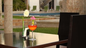 Una mesa con una bebida y una flor en un vaso, una silla y una piscina al fondo.