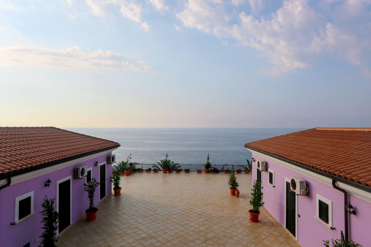 Un edificio con un patio piastrellato e piante in vaso, con vista su un corpo d'acqua.