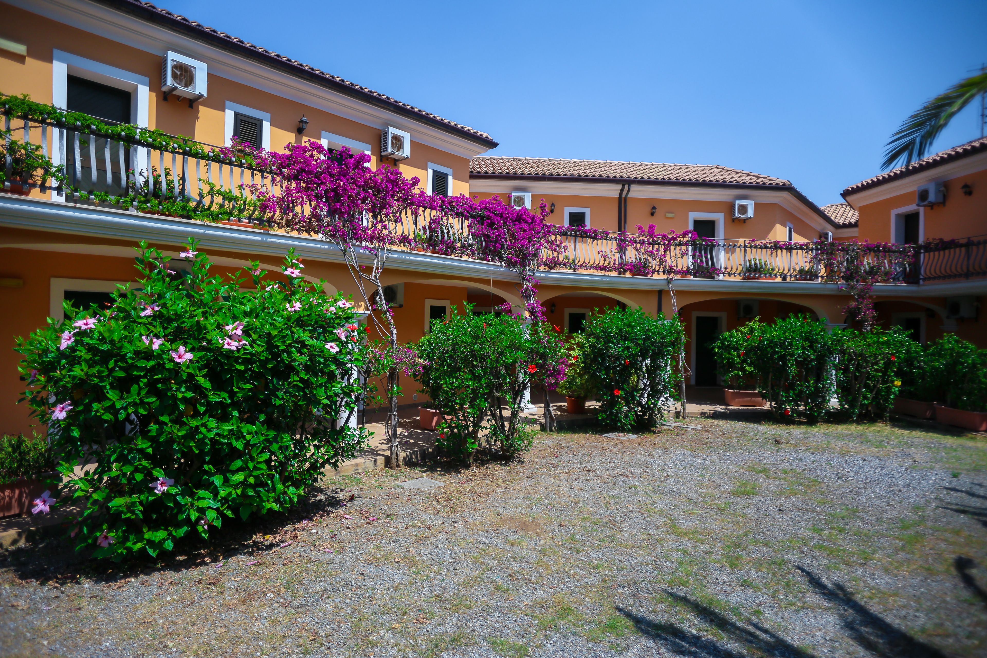 A courtyard with a gravel ground, surrounded by buildings with balconies adorned with flowering plants.