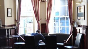 A corner seating area with a table and chairs, a window with curtains, and a framed picture on the wall. - The Crown Hotel (Ryde)