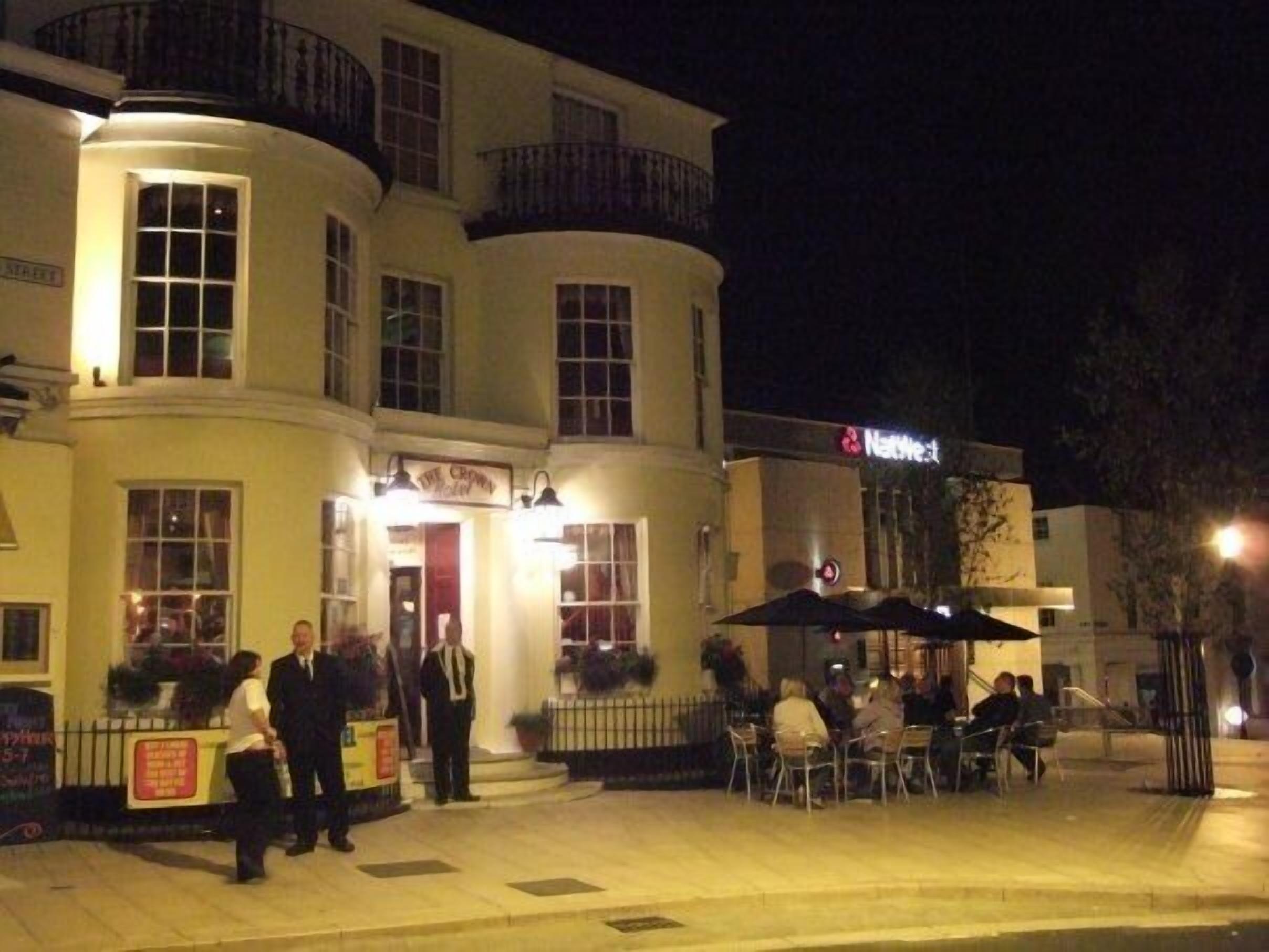 Un hotel con entrada en esquina, zona de estar al aire libre y un cartel visible que dice 'The Crown Hotel'.