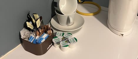 Una mesa blanca con una cafetera, una lámpara, una taza y una caja de cartones de leche.