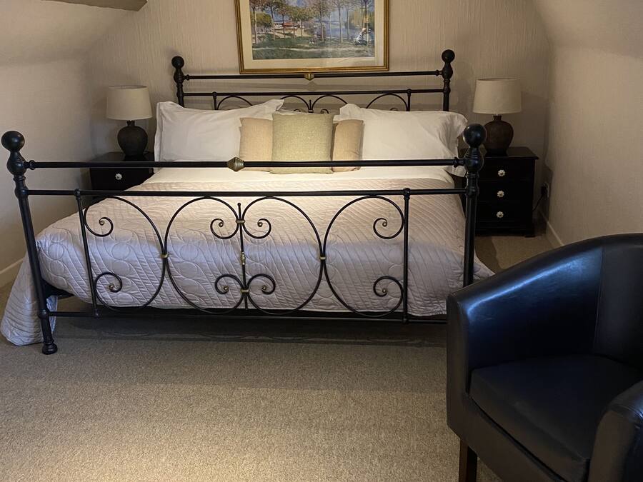 A bedroom with a bed, two bedside tables, a chair, a painting on the wall, and a sloped ceiling.
