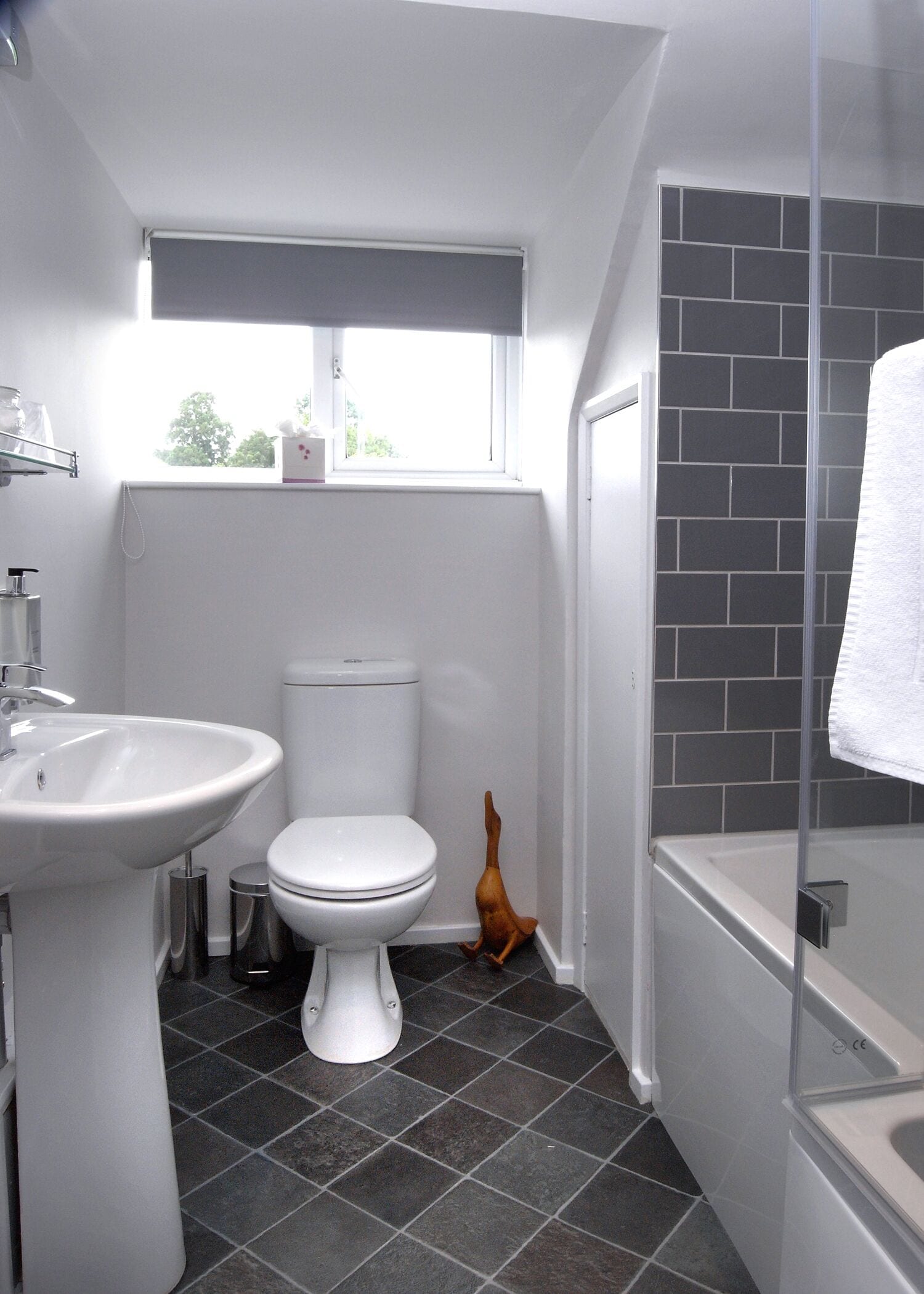 A modern bathroom with a white sink, toilet, and bathtub. There is a window above the toilet and a towel hanging on the bathtub.