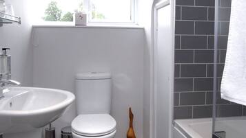 A modern bathroom with a white sink, toilet, and bathtub. There is a window above the toilet and a towel hanging on the bathtub.