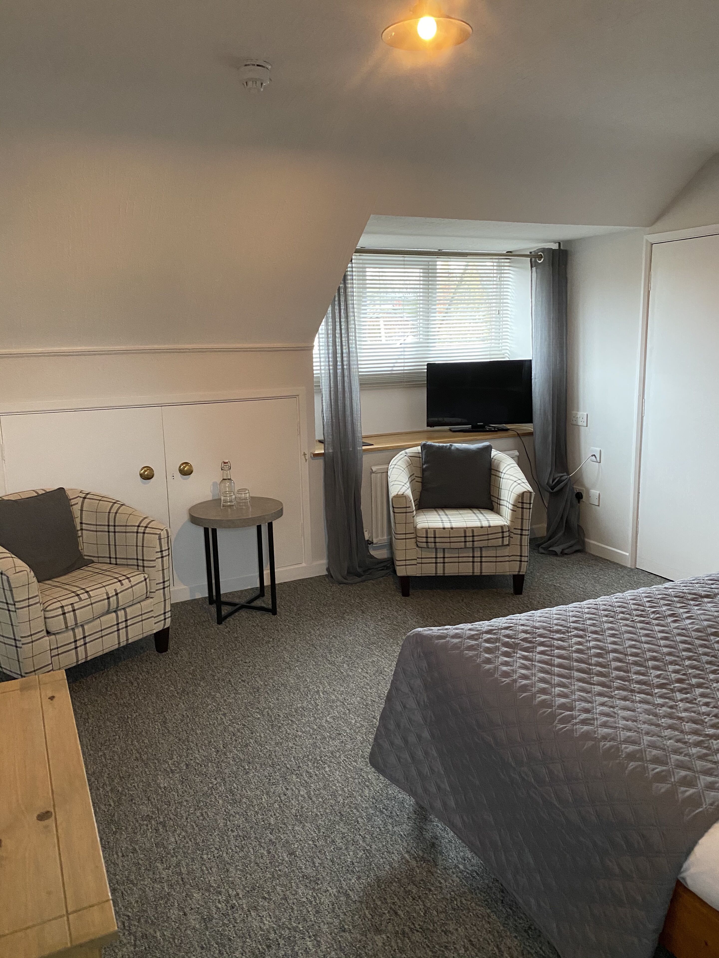 Habitación de hotel compacta con una cama, dos sillones, una mesita, televisor y ventana con cortinas.