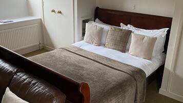 A bedroom with a bed, a brown leather sofa, a window, and framed pictures on the wall.