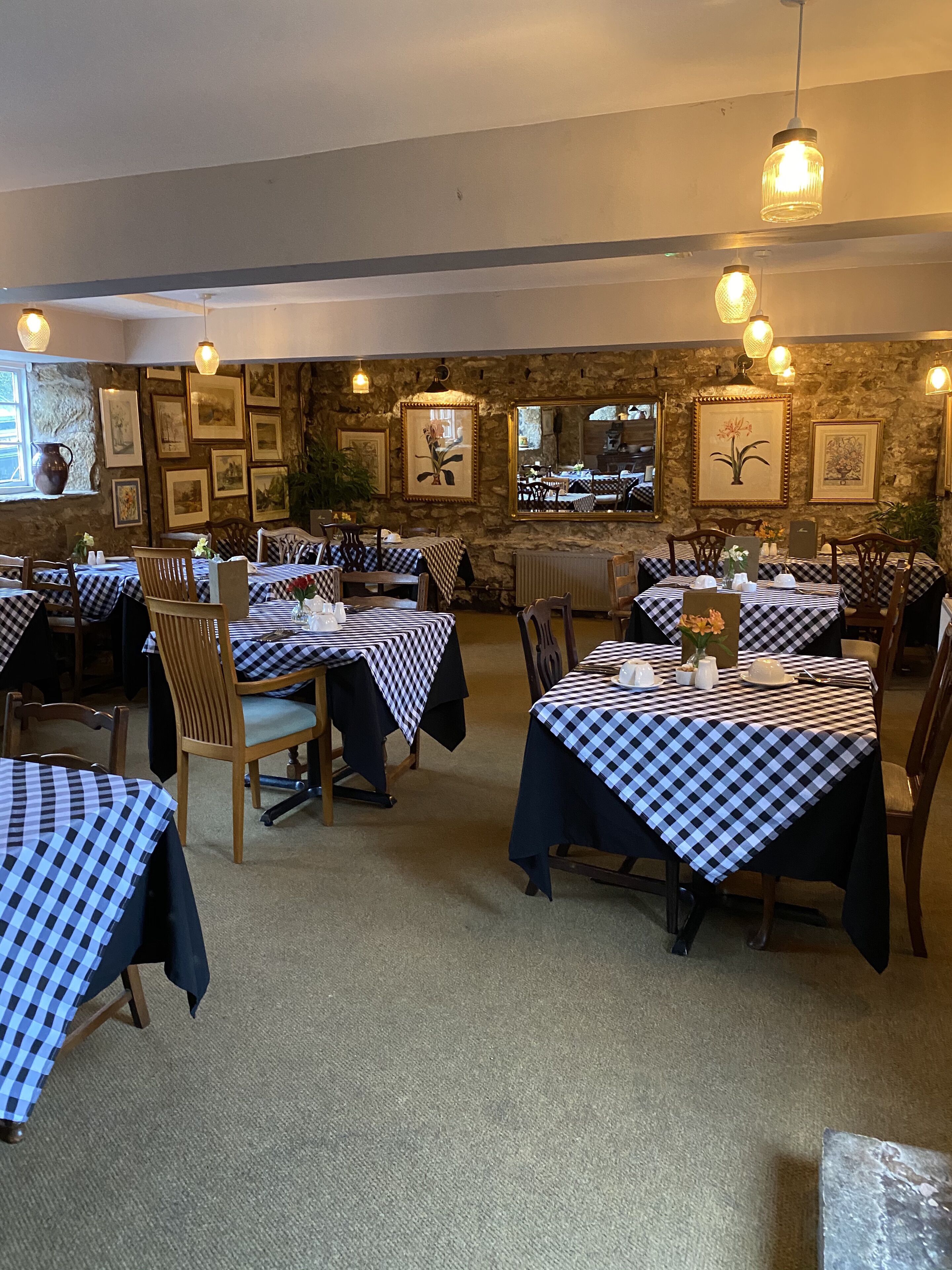 Un restaurante con manteles a cuadros, sillas de madera, cuadros en las paredes y lámparas colgantes.
