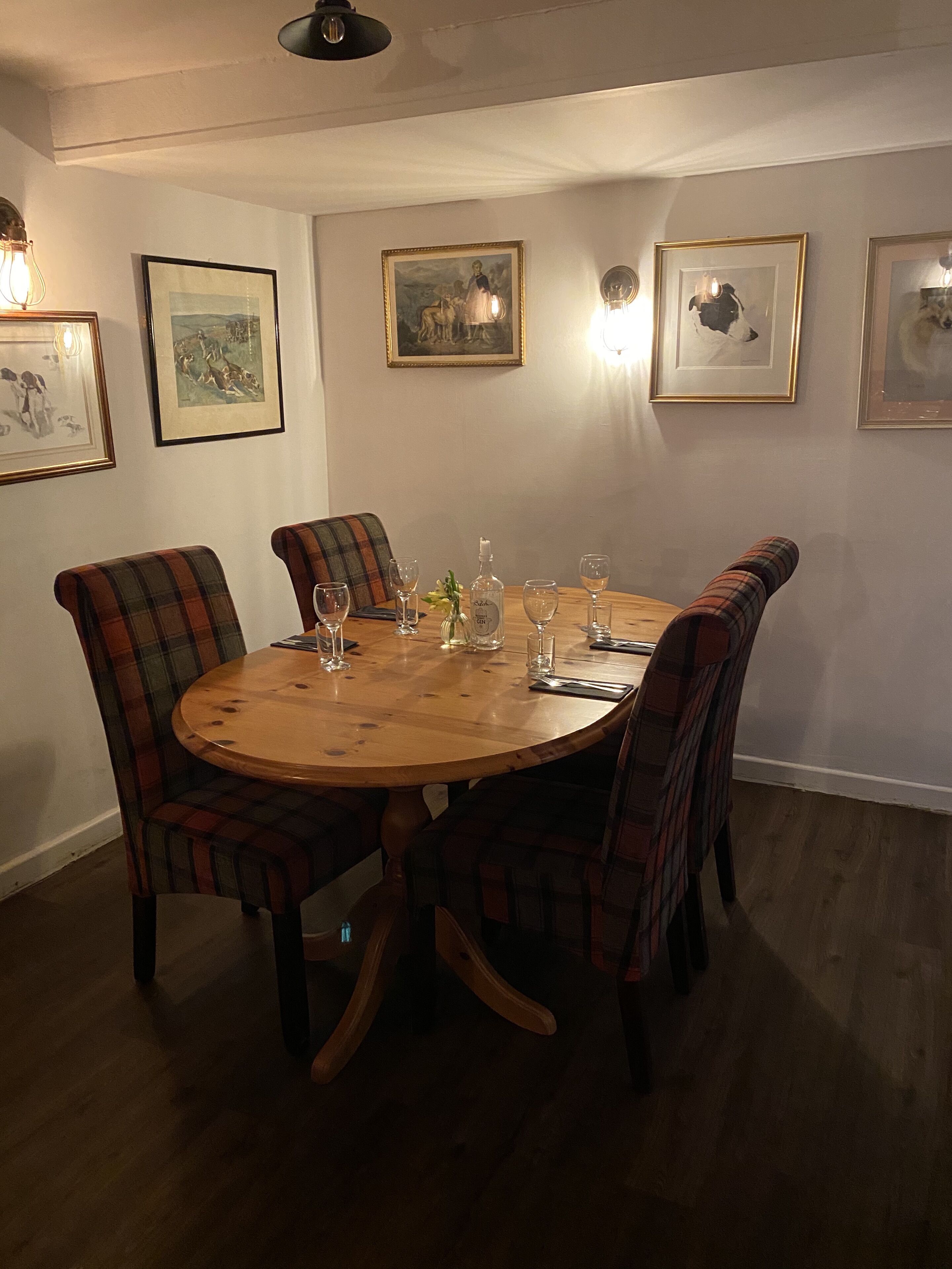 A dining room with a round wooden table, plaid chairs, and framed artwork on the walls.