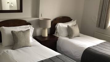 Habitación de hotel con dos camas, una mesita de noche con lámpara, un espejo y una ventana con cortinas.