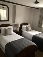 Habitación de hotel con dos camas, una mesita de noche con lámpara, un espejo y una ventana con cortinas.