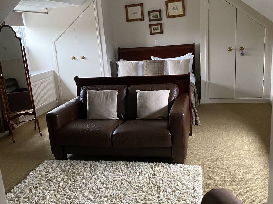 Ein Schlafzimmer mit einem braunen Ledersofa, einem weißen Shag-Teppich, einem Bett mit Holz-Kopfteil und einem weißen Kleiderschrank.