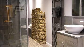 A modern bathroom with a glass shower enclosure, a stone accent wall, and a large sink with a mirror above it.