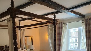 Un lit à baldaquin à quatre poteaux, agrémenté d’un canapé en cuir marron et d’un tapis à motifs floraux.