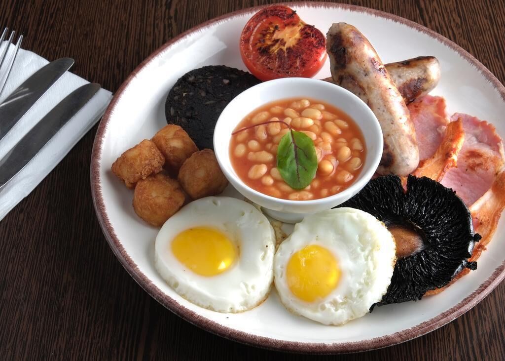 A plate of breakfast food including eggs, beans, sausages, and bacon.