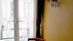 Una habitación con ventana, una silla y una lámpara fijada a la pared.