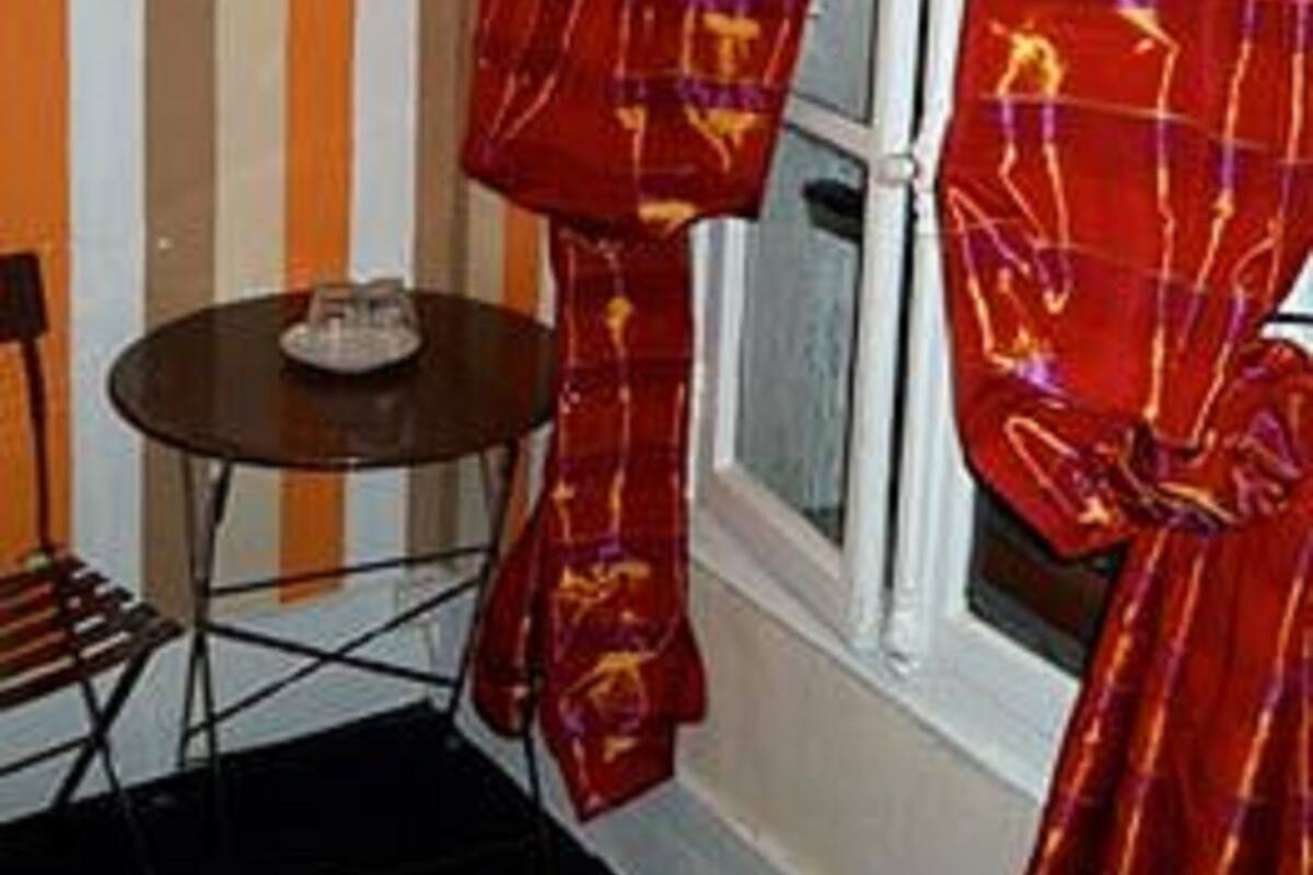 A room with a striped wall, a window with red curtains, a small round table, and a chair.