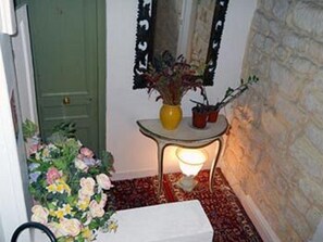 A hallway with a green door, a small table with a vase and potted plants, a lit floor lamp, and a floral arrangement. - Hotel de Lille - Louvre (Paris)