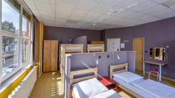 A dormitory room with bunk beds, a desk, a chair, and a window with a view of the street.