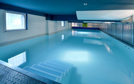 An indoor swimming pool with clear water, a blue ceiling, and a caution sign on the wall.