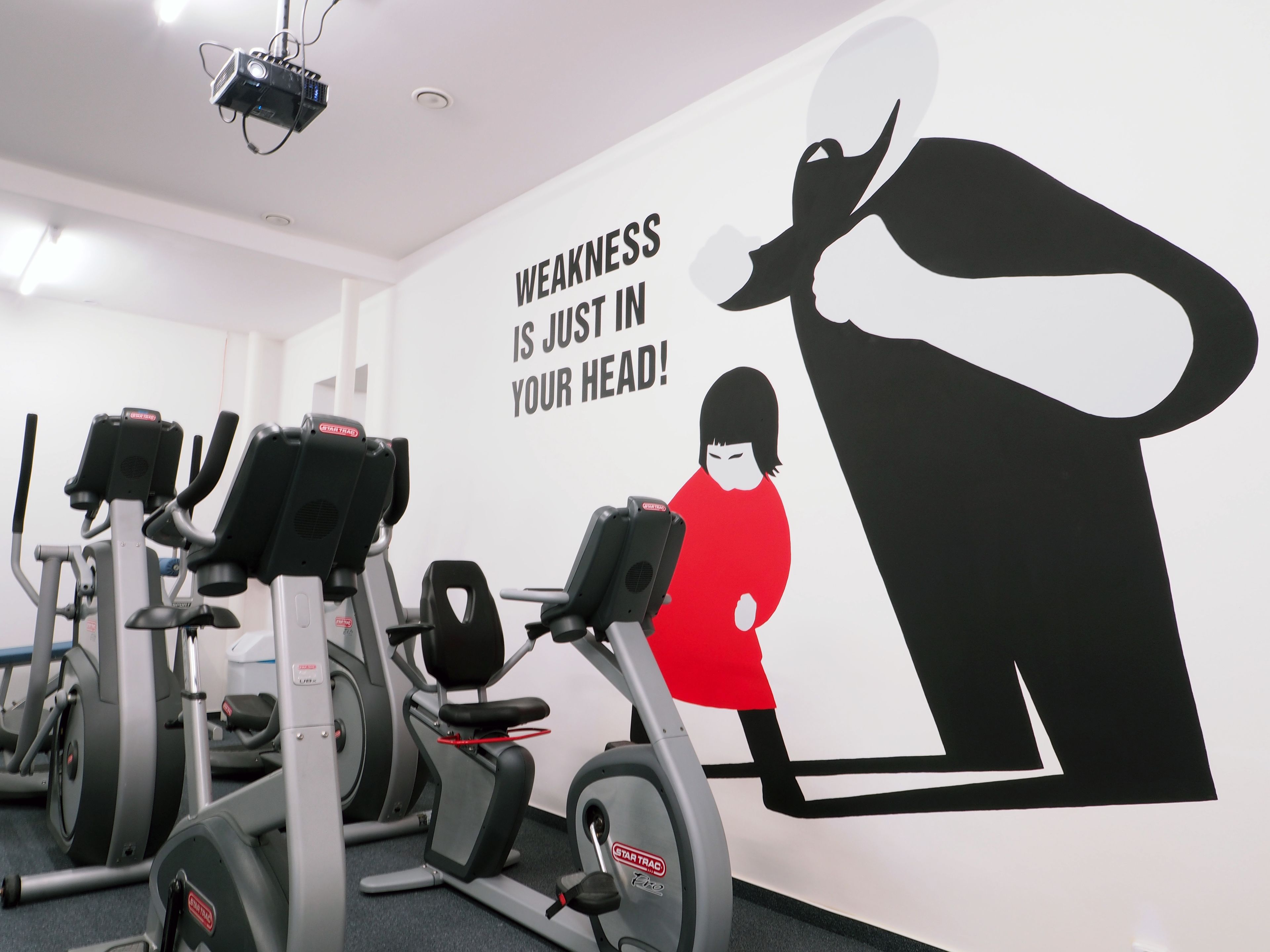 A gym with exercise equipment and a motivational quote on the wall.