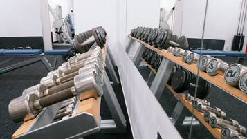 A gym with rows of dumbbells and weight plates, a bench press, and a treadmill.