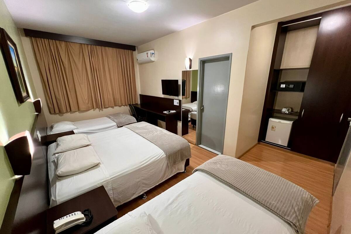 Une chambre d’hôtel avec deux lits, un bureau, une chaise, une armoire, un miroir et une petite kitchenette.