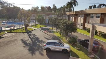 A parking area with a white car, a pool, and a building with multiple windows and air conditioning units.