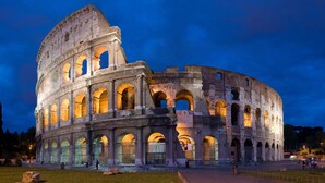 Ein historisches Amphitheater mit zahlreichen Bögen und einem teilweise erhaltenen Mittelteil, umgeben von einer gepflegten Grünfläche.