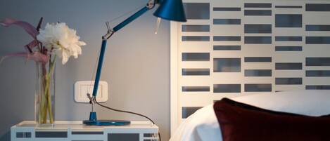 A neatly arranged bedroom with a white bedside table, a blue desk lamp, and a vase with flowers.