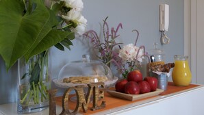 Ein Tisch mit einer Glaskaraffe voller Blumen, einem Holzschild, einer Obstschale, einer Glaskanne und einer Saftflasche.
