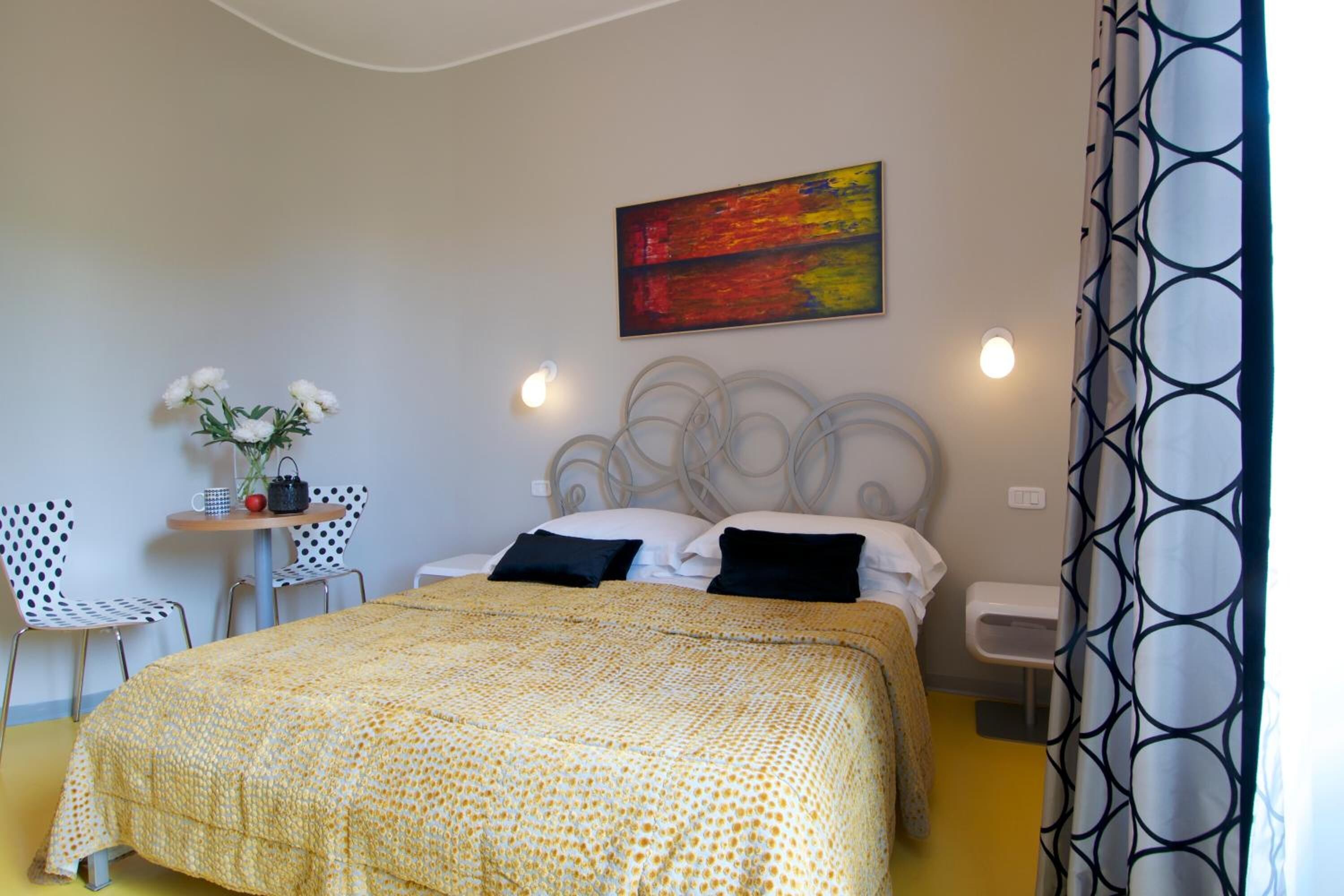 Ein Schlafzimmer mit Bett, Nachttisch, Sessel, kleinem Tisch mit Blumenvase und einem Bild an der Wand.