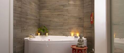 A modern bathroom with a freestanding bathtub, a red decorative stool, and a small plant.