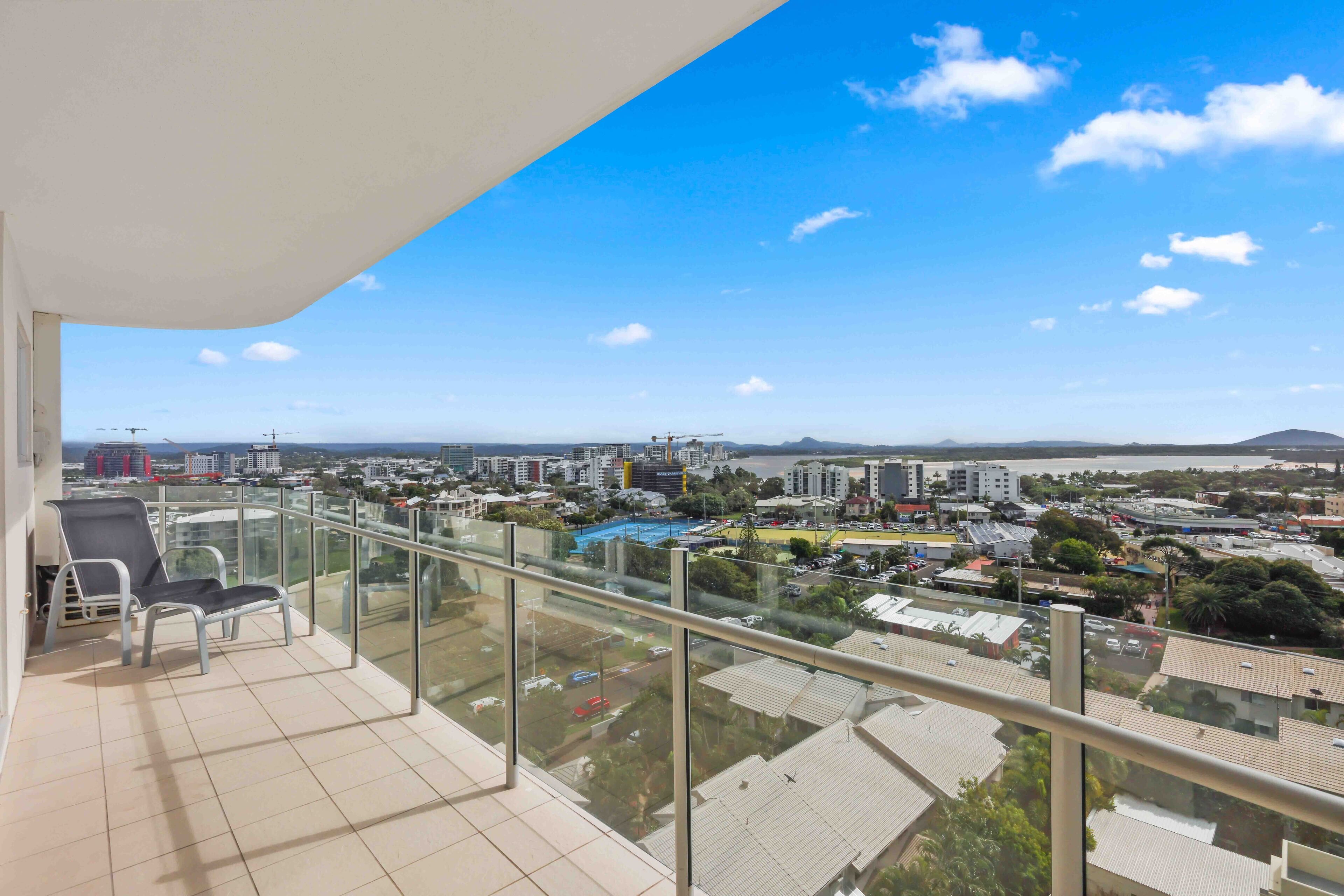 A balcony with a clear view of a cityscape, including buildings, a body of water, and distant hills.