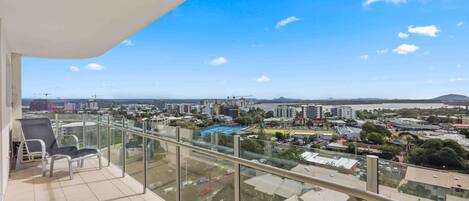 A balcony with a clear view of a cityscape, including buildings, a body of water, and distant hills.