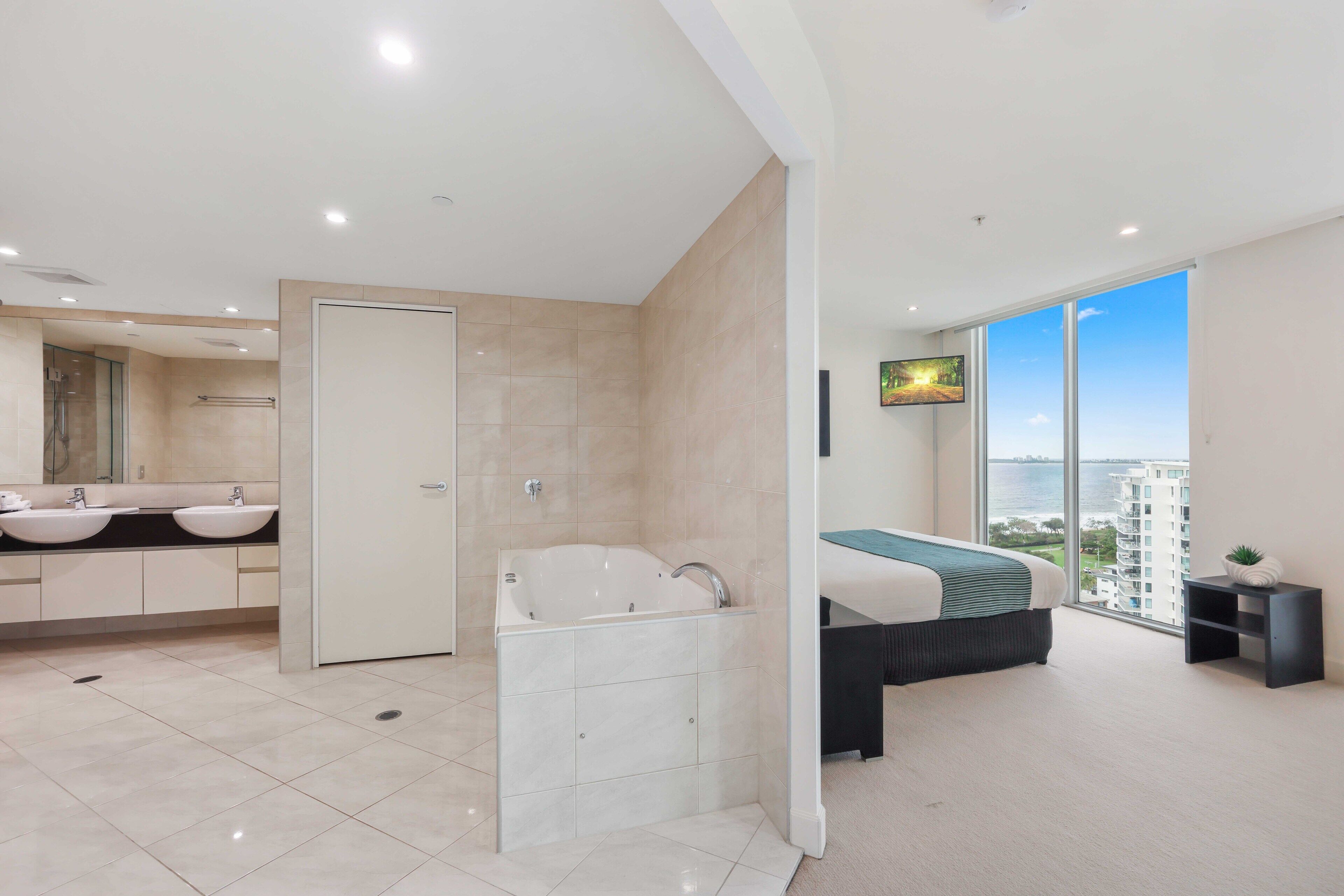 A modern bathroom with a bathtub, two sinks, and a large mirror.