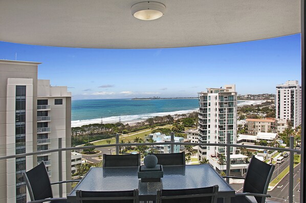 A balcony with a table and chairs overlooking a beach and cityscape.