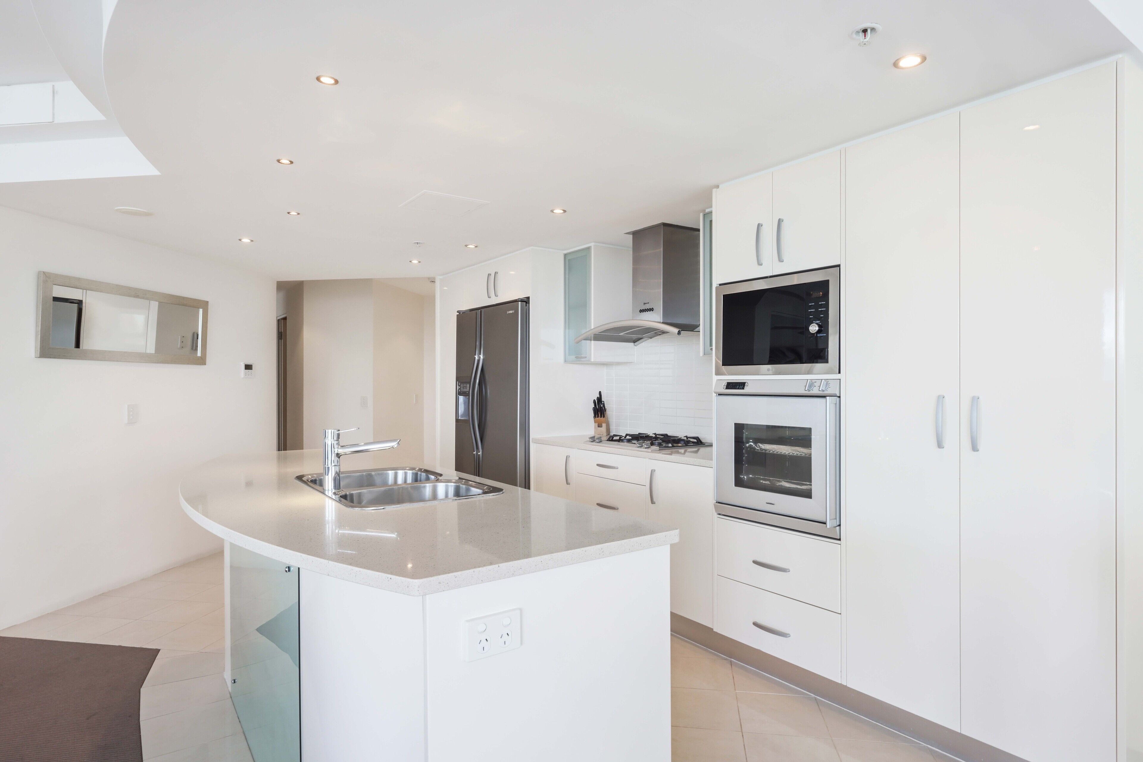 A modern kitchen with white cabinetry, stainless steel appliances, and a central island with a sink.