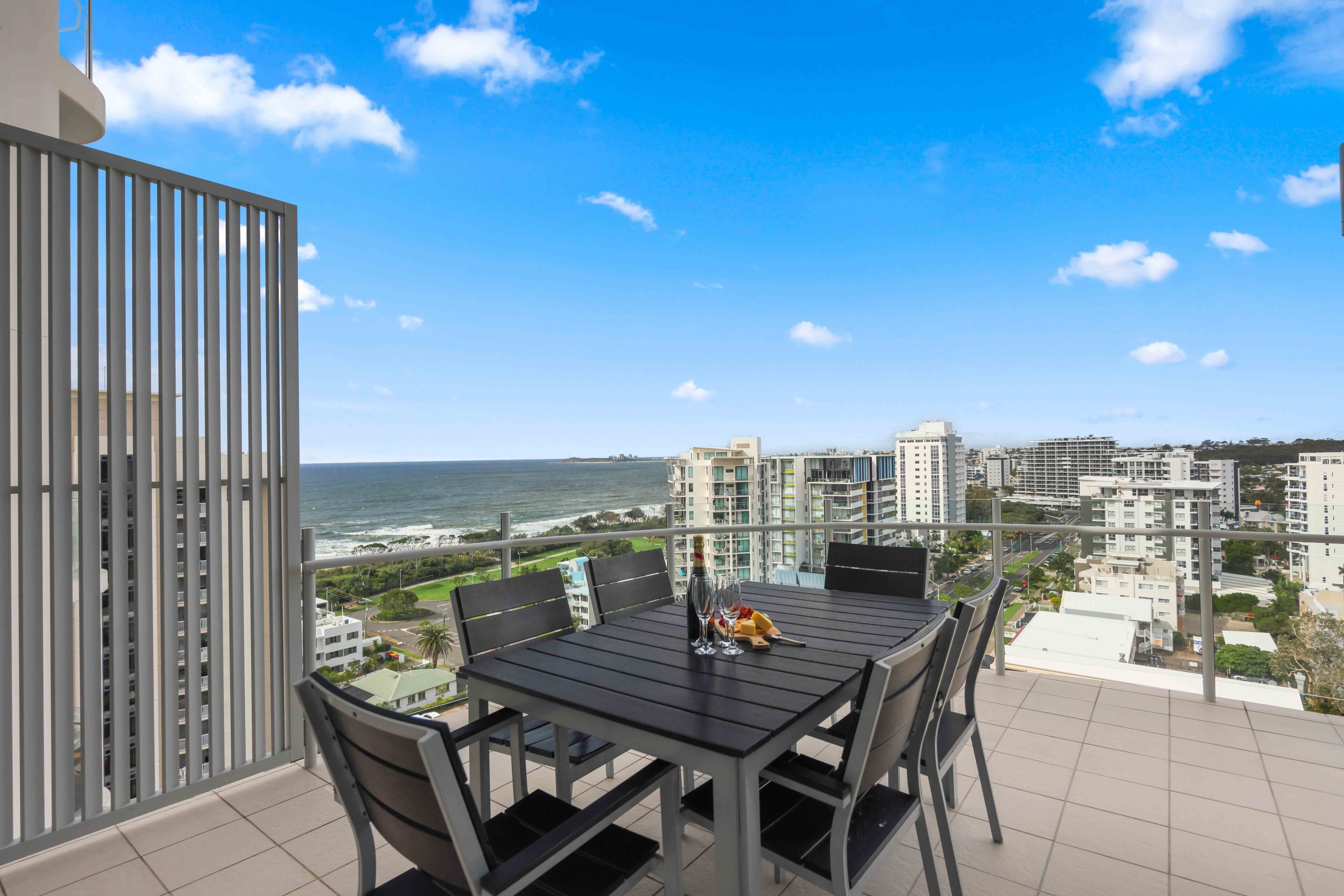 A balcony with a table and chairs, overlooking a coastal cityscape.