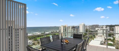 A balcony with a table and chairs, overlooking a coastal cityscape.